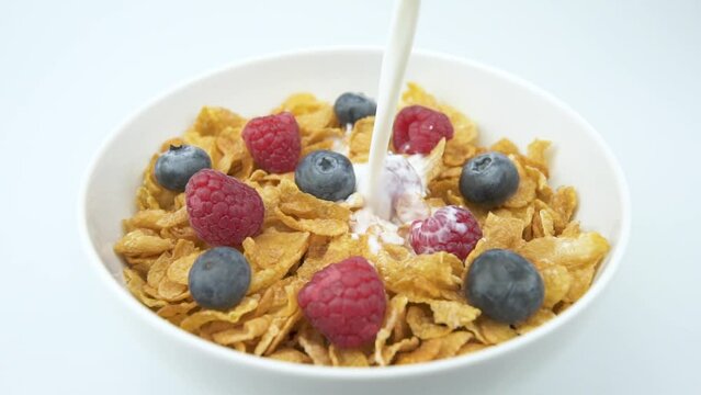 Pouring milk on corn flakes cereals with raspberry and blueberries in a bowl