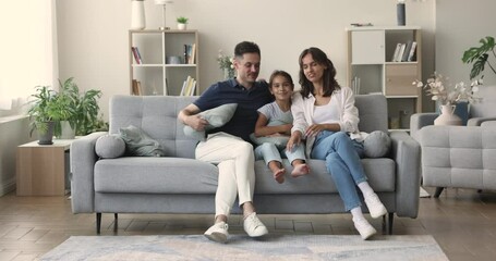 Happy Hispanic couple with little 10s pretty daughter sitting on comfortable couch smile look at camera, spend time together at own or rented house. Bank mortgage for young family, tenancy, adoption