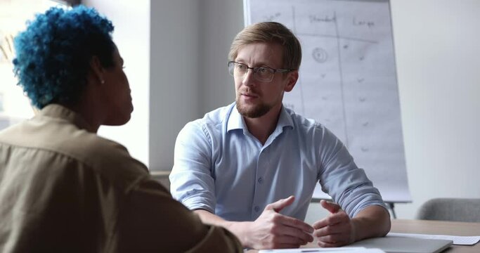 Two multi racial colleagues lead conversation met in company office. Businessman make speech, share strategy to partners, speak about joint project, pass job interview, talking to African HR manager