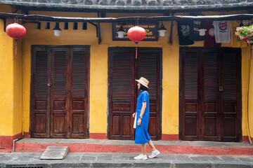 Tourists wearing blue dresses walk in front of shops painted in yellow, sightseeing in the old city of Dalat, Vietnam.