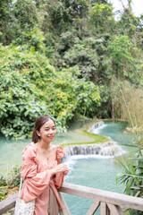 Young Asian woman standing on the wooden walkway in the Kuang Si Waterfall Popular attractions of Lung Prabang, Laos