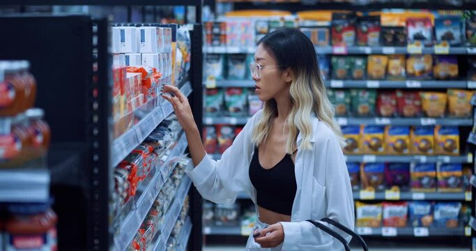 Portrait of female shopper in a grocery store chooses products looks at the best price while shopping in a grocery supermarket. Young asian woman with a basket in hand chooses food in a grocery store