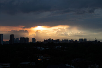 Warm sunset after rain with dark clouds above and silhouette of tall buildings and houses in foreground