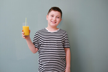 A cute cheerful boy in yellow tee shirt holding a glass of orange juice on green background.