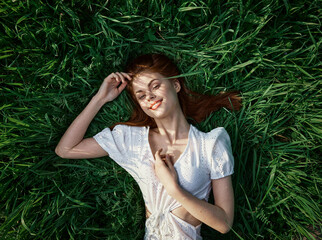 an elegant woman in a light dress lies in the grass and enjoys life