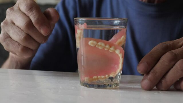 the old man takes out of his mouth puts removable dentures in a glass, selective focus. hygiene and care for dentures dental implantation, be healthy