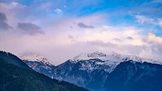 time lapse shot of monsoon clouds moving over snow covered himalaya mountains with the blue orange sunset sunrise light over kullu manali valley India