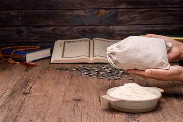 Hands holding a wooden bowl of rice grains and money bag for zakat, Islamic zakat concept. Muslims help the poor and needy. Conceptual shoot for property, income, and fitrah zakat.
