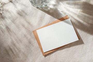 Empty paper card with mock up copy space on beige table surface with aestethic sunlight shadows,...
