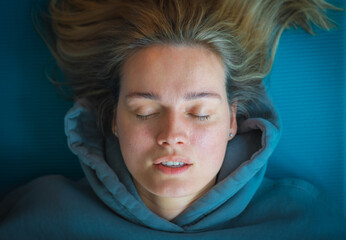 Portrait of a beautiful blond Caucasian girl with a blue sweatshirt lying on a mat, breathing and...