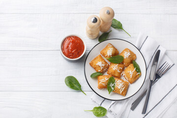 Deep fried traditional italian dish ravioli dumplings stuffed with spinach and cheese served with marinara tomato dipping sauce closeup on the wooden table. Horizontal top view from above