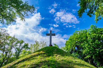 Fototapeta na wymiar Christian cross on a mound against a blue sky with white clouds. Christian symbol. Religion and culture. Ukrainian Orthodox Church. Catholicism and Protestantism. Place of crucifixion. Easter.
