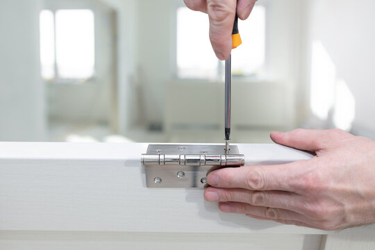 Worker installs a door hinge on a door using a screwdriver. Screw tightening. Repair in the house. Door installation. Close-up.