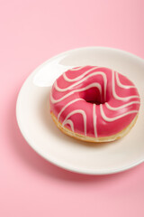 Tasty pink glazed strawberry donut on white round plate from above on pink background. Fast snack time.  