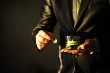 Businessman hand putting money (coin) in the glass jar, vintage tone effect