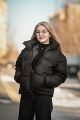 Portrait of a young beautiful blonde girl in glasses on a spring sunny day in an urban environment.