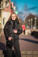 Portrait of a young beautiful blonde girl in glasses on a spring sunny day in an urban environment.