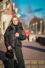 Fototapeta premium Portrait of a young beautiful blonde girl in glasses on a spring sunny day in an urban environment.