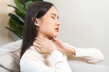 Obraz na płótnie Canvas Body muscles stiff problem, asian young attractive woman, girl pain with neck pain ache from work, holding massaging rubbing shoulder hurt or sore, painful sitting on sofa at home. Healthcare people.