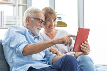 Happy husband and wife senior couple elderly family, caucasians mature, adult lover and retired man, woman using tablet communicating, shopping online, reading news on sofa at home together.