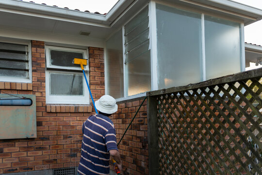 Man washing outside window with long pole and brush. Auckland