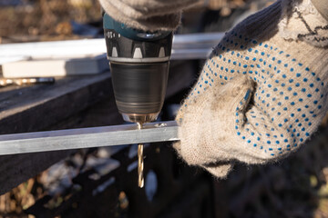 A master in work gloves is holding a metal drill and drills off the aluminum profile. Detailed...
