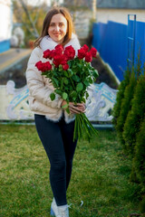 Fototapeta premium A woman in a white jacket stands on a lawn with a bouquet of red roses.