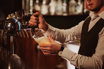 hands of bartender pour into glass draught light foamy beer from tap in bar