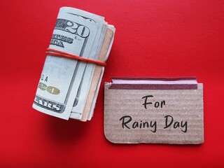 Cash dollars money on red background with handwritten text card FOR RAINY DAY, concept of saving emergency fund for tough time