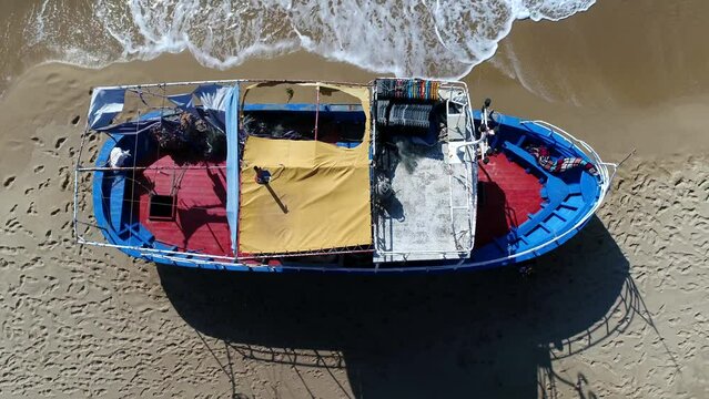 Aerial top down drone view of refugee boat showing the colourful painted hull and footprints all around the ship typical scene of Greek or Italian beach during refugee-crisis 4k high resolution