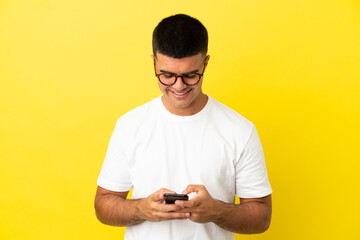 Young handsome man over isolated yellow background sending a message with the mobile