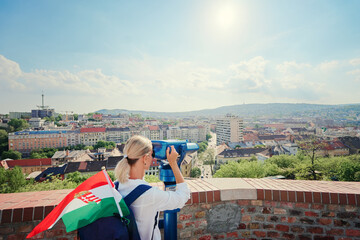 Young traveling woman enjoying the view usin coin-operated street binocular in Budapest, Hungary.