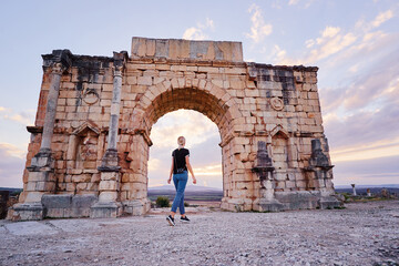 Happy young woman walking on ancient antique city Volubilis. Traveling by Morocco. - obrazy, fototapety, plakaty