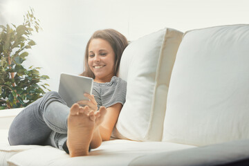 Woman sitting on couch, casually dressed, using tablet with long