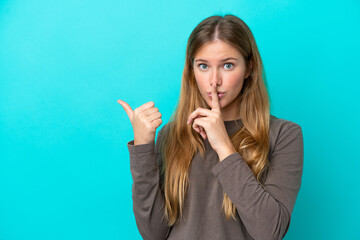 Young blonde woman isolated on blue background pointing to the side and doing silence gesture