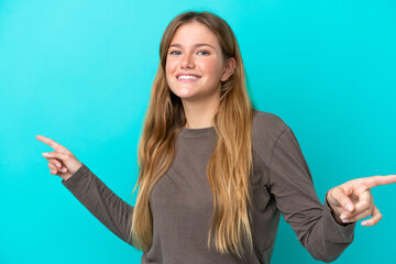 Young blonde woman isolated on blue background pointing finger to the laterals and happy