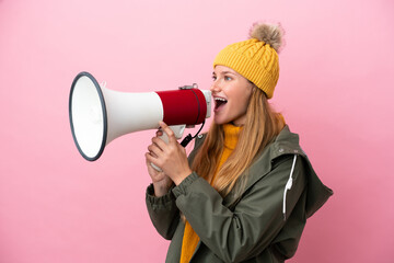 Young blonde woman wearing winter jacket isolated on pink background shouting through a megaphone