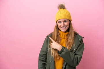 Young blonde woman wearing winter jacket isolated on pink background pointing to the side to present a product