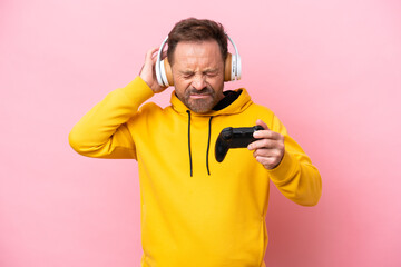 Middle age man playing with a video game controller isolated on pink background frustrated and covering ears