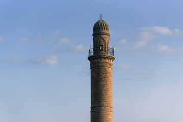 A single yellow sandstone minaret against a blue sky with small clouds in Mardin. Turkey