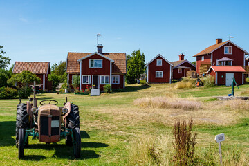 Obraz premium An old tractor, red houses and a communal hand water pump in a small village on the island of Harstena in the Gryt archipelago in the Baltic Sea