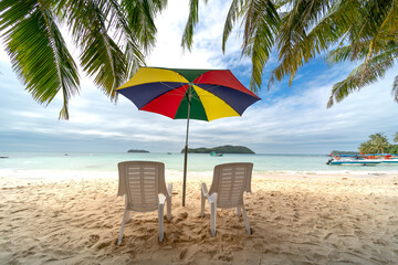 White beach chairs and full color stand umbrella on the white sand beach with blue ocean background.