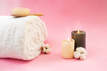 Fototapeta na wymiar Rolled white towel, wooden hair brush, cotton flowers and lit candles