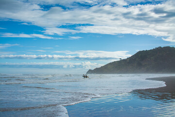 Fototapeta na wymiar A pair of surfers walking into breaker water at Makorori Beach, mist rising over water obscuring distant mountains. Gisborne, New Zealand