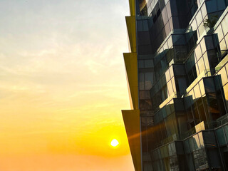 glass curtain building with modern architecture in front of beautiful warm sunset landscape in orange sky and sun view background