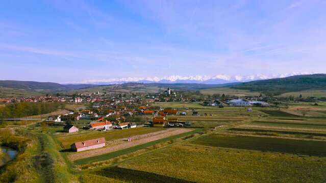 Aerial view over the countryside in Romania at Hosman village, with the fortified church and mountains in the background. Footage was shot from a drone at a lower altitude while flying forward.