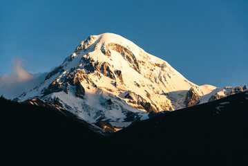 The snow-capped peak of Mount Kazbegi against a clear blue sky is one of the highest mountains in Georgia.