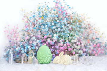 candle amulet in egg and rabbit form, crystals, flowers on table close up, blurred light...