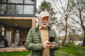 One senior man stand in front of tiny house in day use smart phone