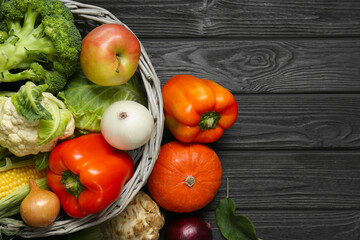 Different fresh vegetables in wicker basket on black wooden table, top view and space for text. Farmer harvesting